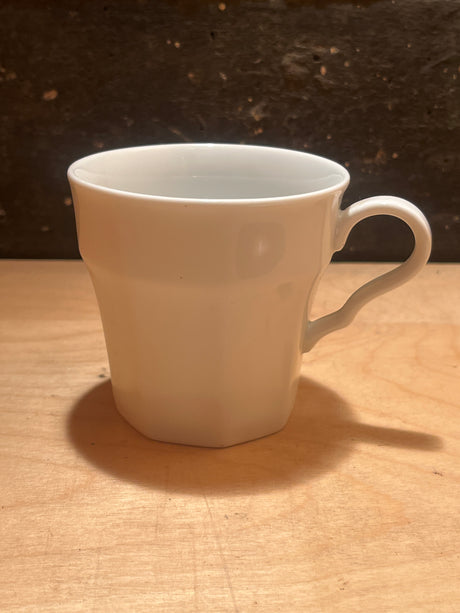 White ceramic octagonal mug from the Savoir Vivre Maison Blanche line, featuring a faceted lower body and curved handle on a wooden surface.