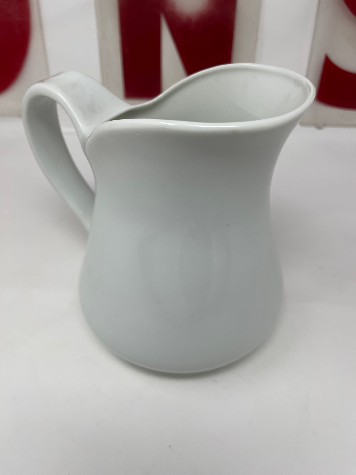 White ceramic pitcher on a white surface, holding approximately 32 fluid ounces, with a small black spot inside. Ideal for serving cold beverages.