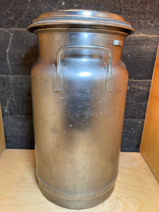 Vintage John Wood Young’s Dairy stainless steel milk can featuring a stamped logo, carrying handles, and a removable lid, reflecting a classic dairy accessory design.