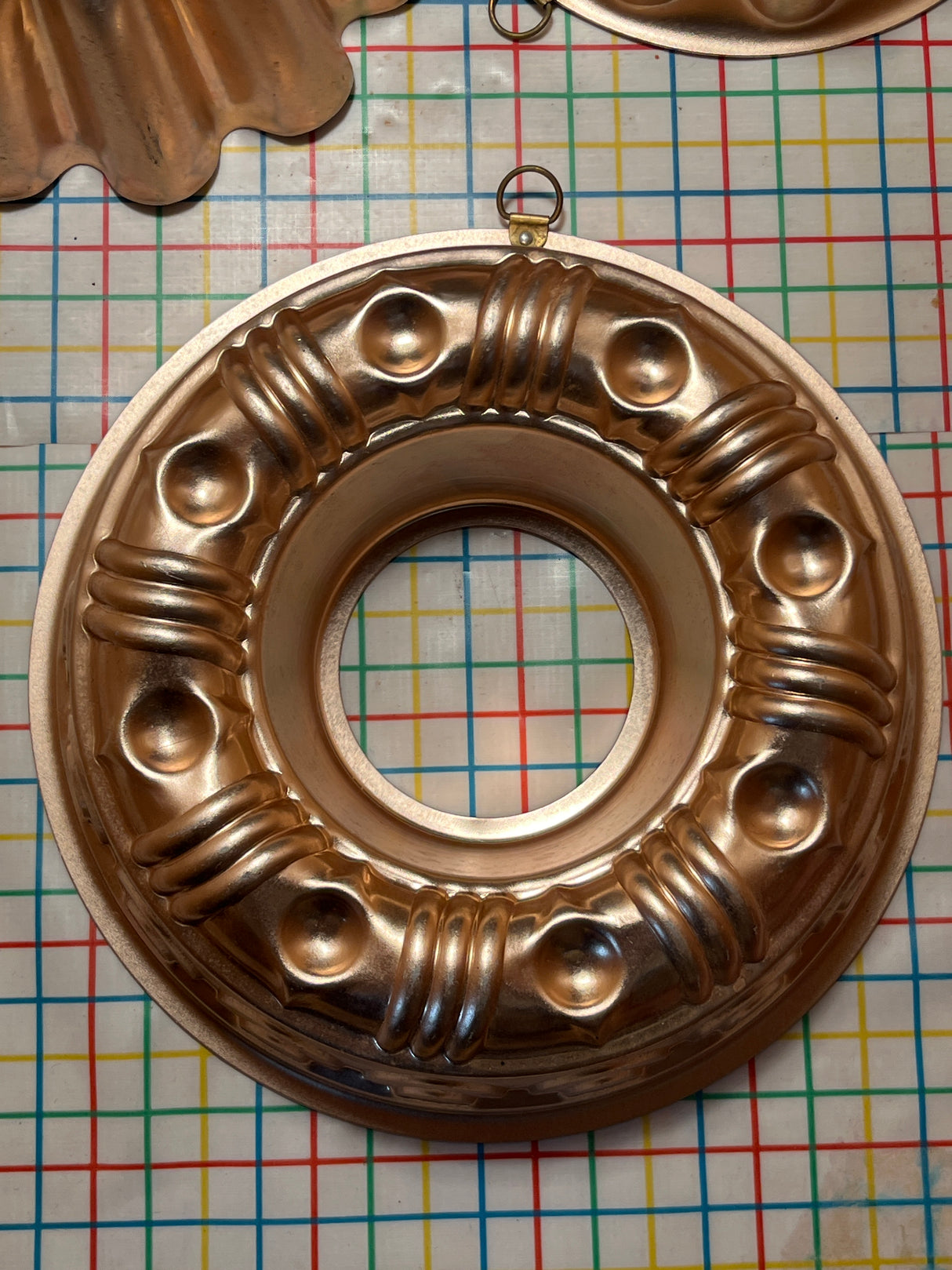 Copper-lined aluminum mold for jello, gelatin, cakes, featuring decorative raised bumps, fluting, and hanging loops, displayed on a textured surface for added elegance.