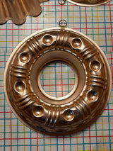 Copper-lined aluminum mold for jello, gelatin, cakes, featuring decorative raised bumps, fluting, and hanging loops, displayed on a textured surface for added elegance.