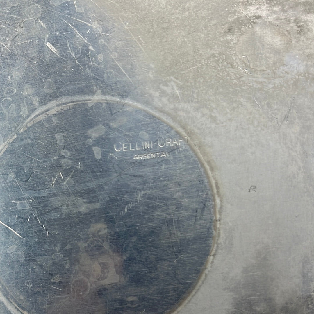 Close-up of a vintage aluminum casserole carrier, showcasing intricate detailing on handles and lid knob, set against a metal surface.