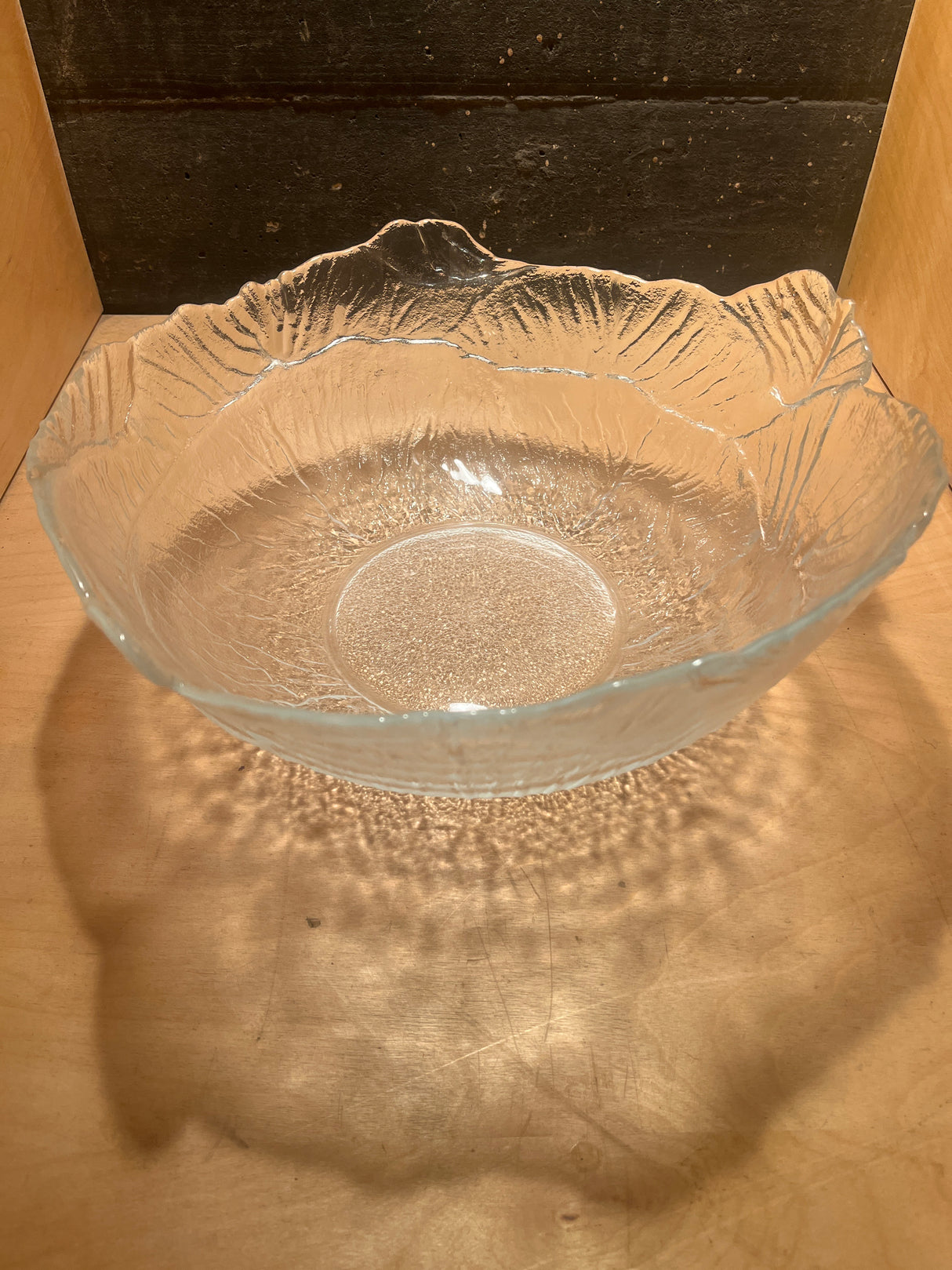 Viking 2408 cabbage 12 glass serving bowl with wavy, textured, clear glass, casting delicate shadow patterns on a wooden surface, ideal for springtime salad presentation.
