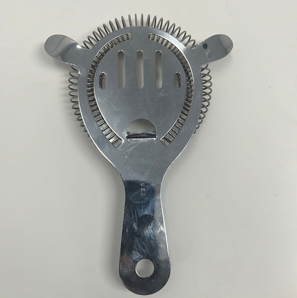 A metal cocktail strainer with two prongs and a handle, resembling a face, a versatile tool for bartending.