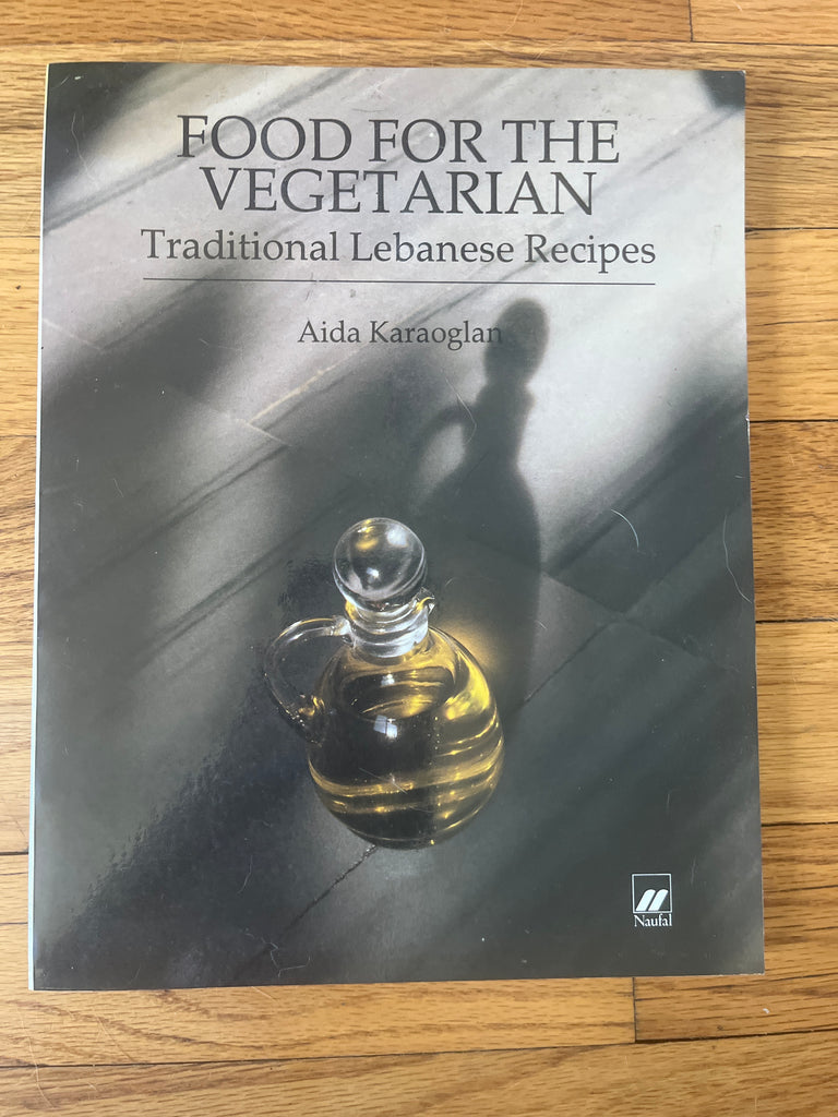 Food for the Vegetarian: Traditional Lebanese Recipes by Aida Karaoglan placed on a table with a glass jug of yellow liquid beside it.