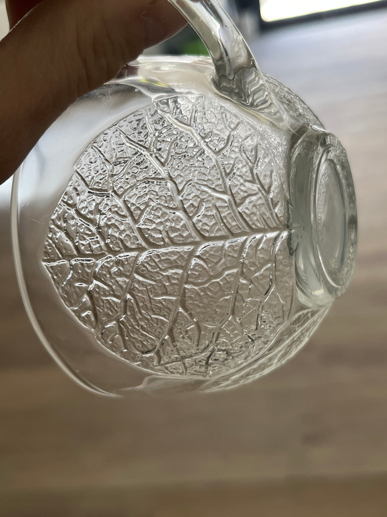 Punch bowl set with leaf pattern embossment, featuring a close-up of a hand holding a glass cup from the set, highlighting its intricate design.