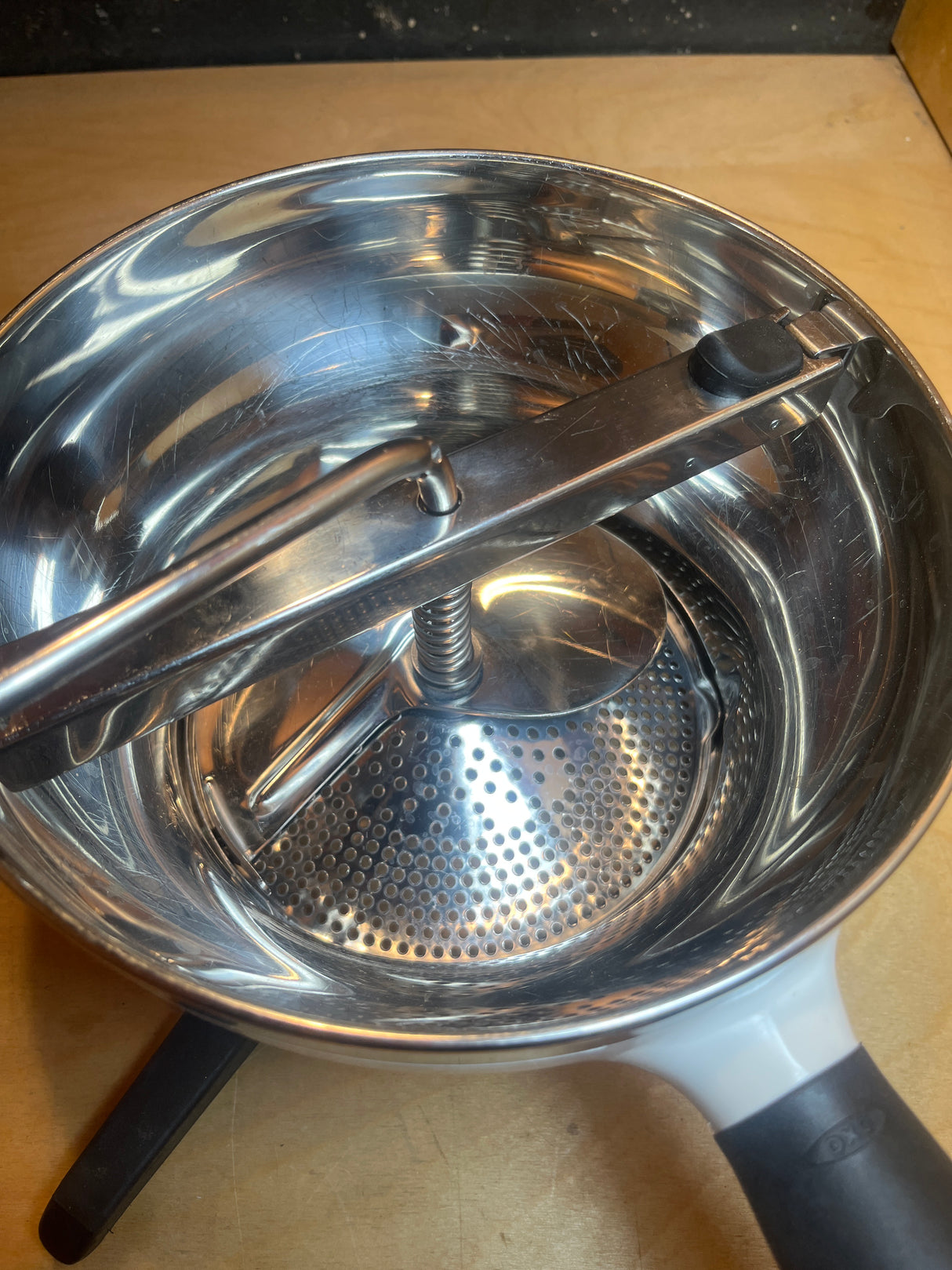 Stainless Steel Food Mill For Purees, Silver and White - OXO Good Grips, shown with crank handle and non-slip legs on a pot, ready for use.