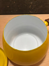 Fondue pot - vintage enamel sunshine yellow with wood handles, featuring a small round shape, white interior, and matching lid, resting on a wooden surface.