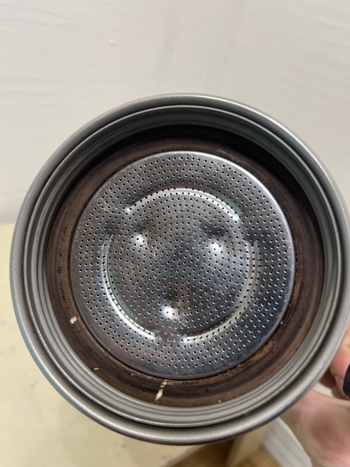 Close-up of a VEV Vigano Carioca 6-cup stainless steel espresso pot's perforated filter plate, showing coffee residue and old rubber gasket.