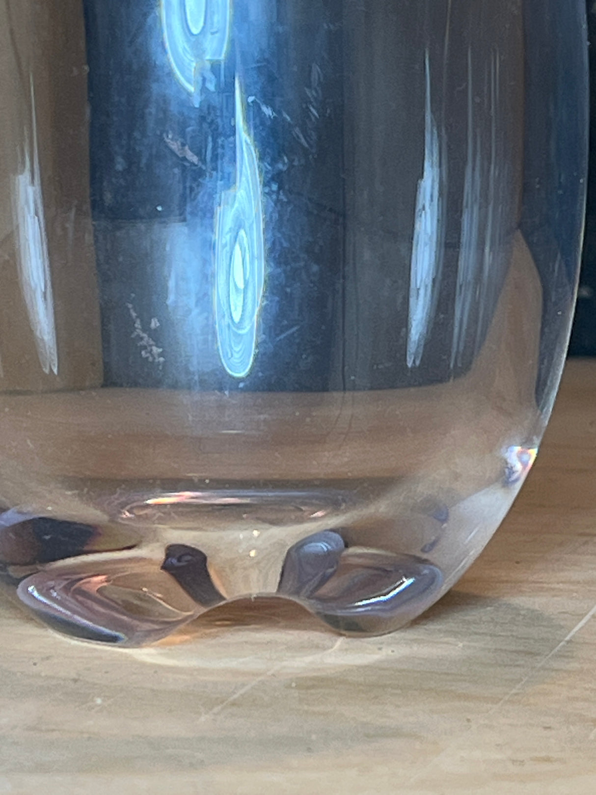 Close-up of the base of a Stemless hard acrylic wine glass, showcasing its indented pattern and light reflections on a wooden surface.