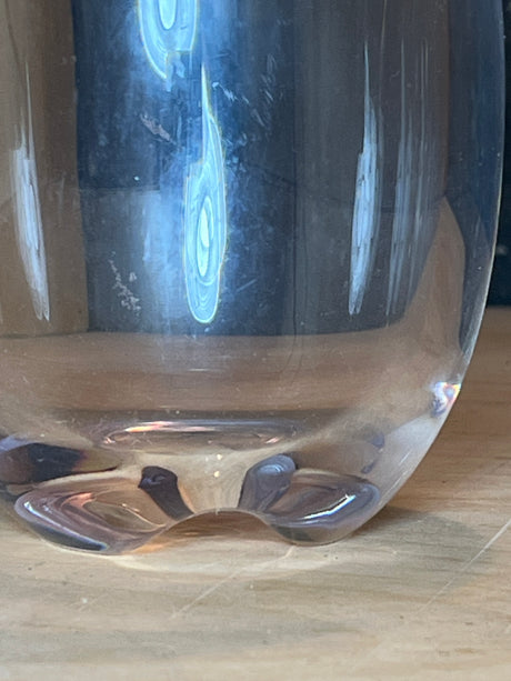 Close-up of the base of a Stemless hard acrylic wine glass, showcasing its indented pattern and light reflections on a wooden surface.