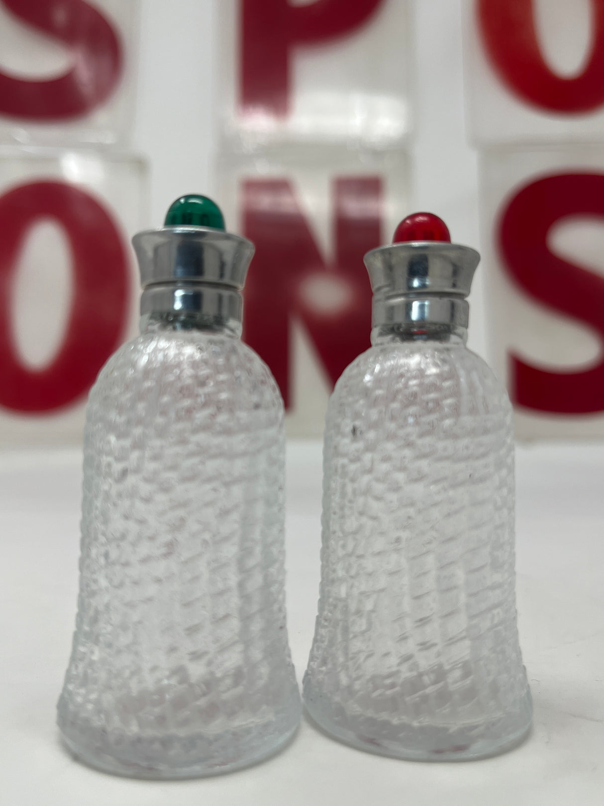 1950s red and green glass salt and pepper shaker set with textured glass, featuring metal hardware, displayed indoors on a table.