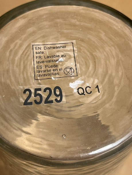 Hammered glass tumbler underside showing dishwasher-safe label in English, French, Spanish, along with stickers reading 2529 and a round QC 1 quality-control label.