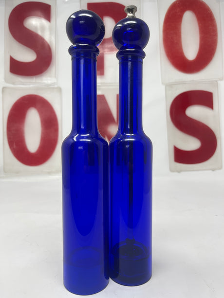 Cobalt blue Olde Thompson salt shaker and pepper grinder set made of translucent lucite, featuring a carbon steel grinder, shown in a close-up view.