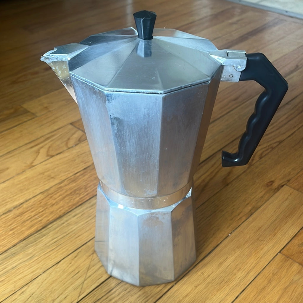 A 12-cup Primula espresso moka pot on a wood floor, featuring a metal surface. Ideal for late-night study sessions or brunch, with minor stains from use.