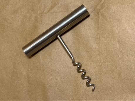 Stelton stainless steel minimalist corkscrew with a T-handle and metal spiral, displayed on a brown surface, showcasing its sleek and functional design.