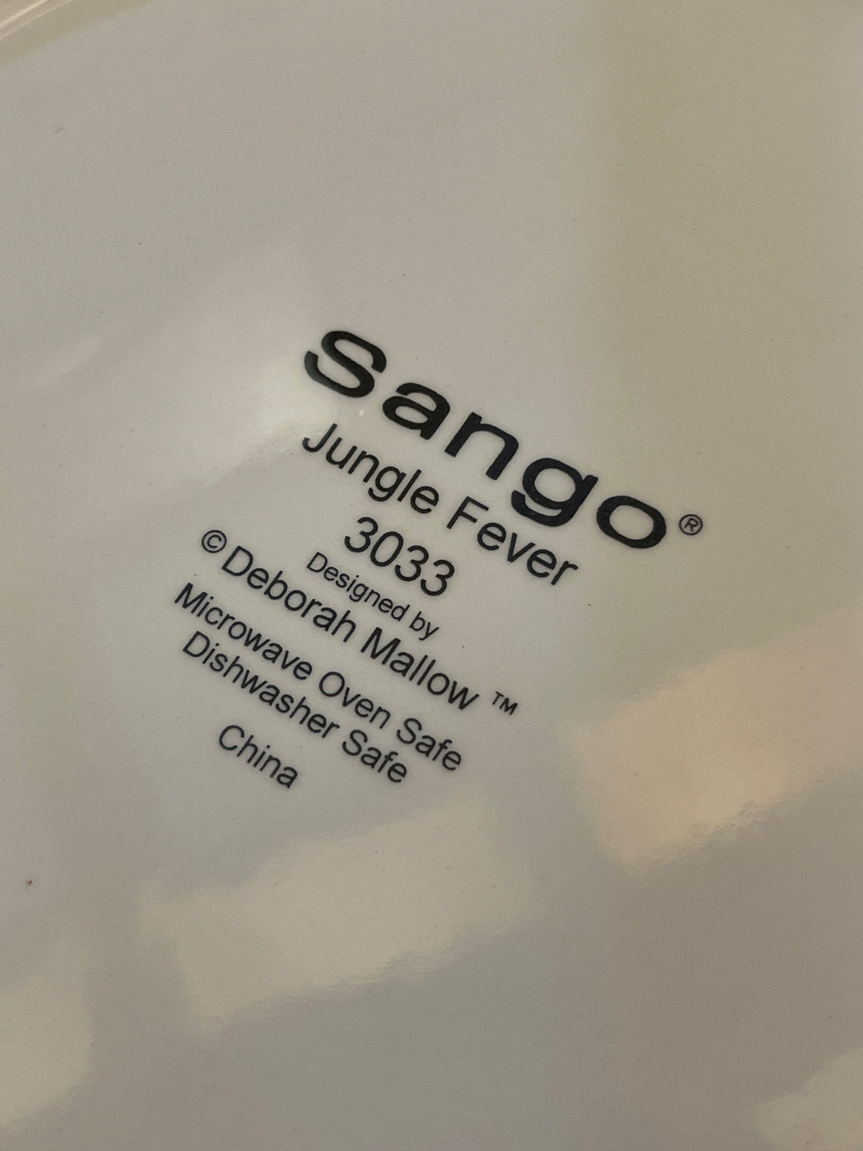 Back-stamp on Jungle Fever dinner plate by Sango 3033, designed by Deborah Mallow, indicating microwave and dishwasher safety, with a description of various animals.