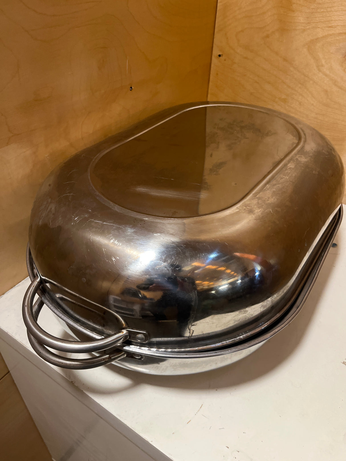 Stainless steel oval roasting pan with rack and lid, featuring a domed lid, loop-style handles, and a slightly scuffed, reflective surface, resting on a countertop.