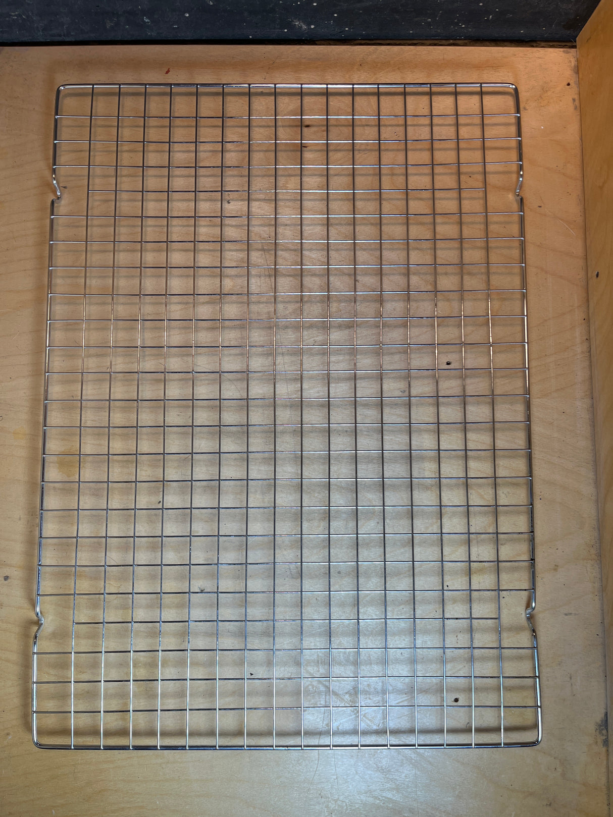 Wire cooling rack - 20 x 14.5 stainless steel, featuring a sturdy grid on elevated feet, perfect for cooling baked goods on a wooden surface.