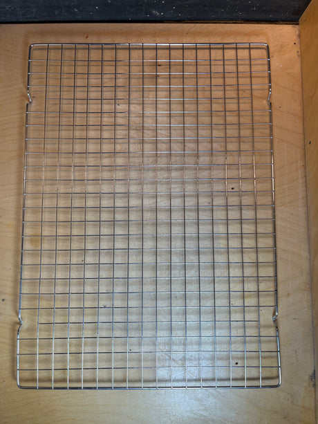 Wire cooling rack - 20 x 14.5 stainless steel, featuring a sturdy grid on elevated feet, perfect for cooling baked goods on a wooden surface.
