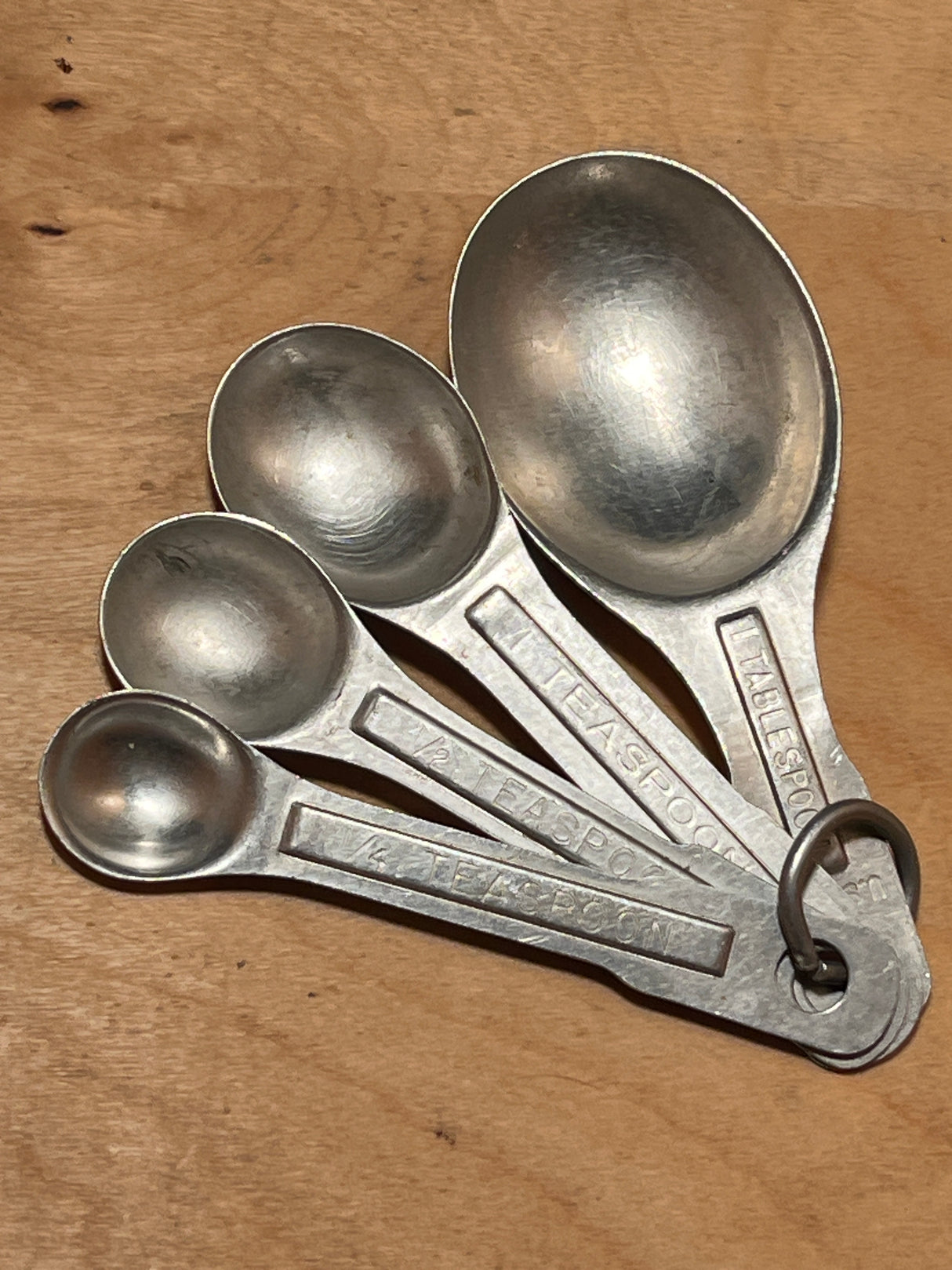 Measuring spoons - set of 4 vintage aluminum, featuring 1 Tbsp, 1 tsp, ½ tsp, and ¼ tsp, connected by a ring on a wooden surface.