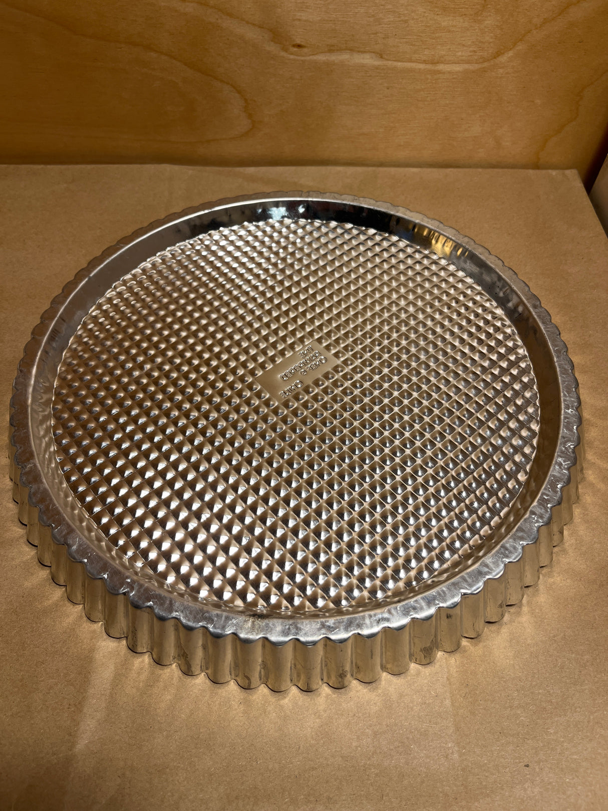 Pampered Chef stainless steel flan pan, round with fluted edges and removable, textured bottom, ideal for even baking and easy release of flans or quiches.