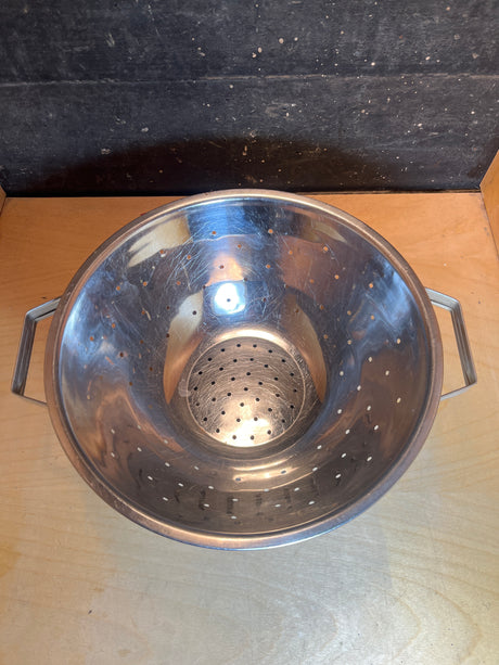 Colander - vintage stainless steel on wooden countertop, perfect for washing small portions. Geometric design adds vintage charm, ideal for rinsing pasta or vegetables.
