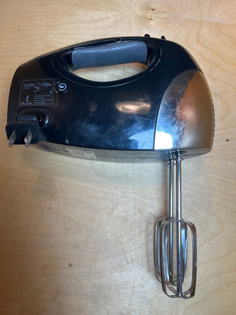 Hand mixer - Oster 6-speed 2577 with retractable power cord, shown on a wooden surface with attached wire beaters, highlighting its compact and efficient design.