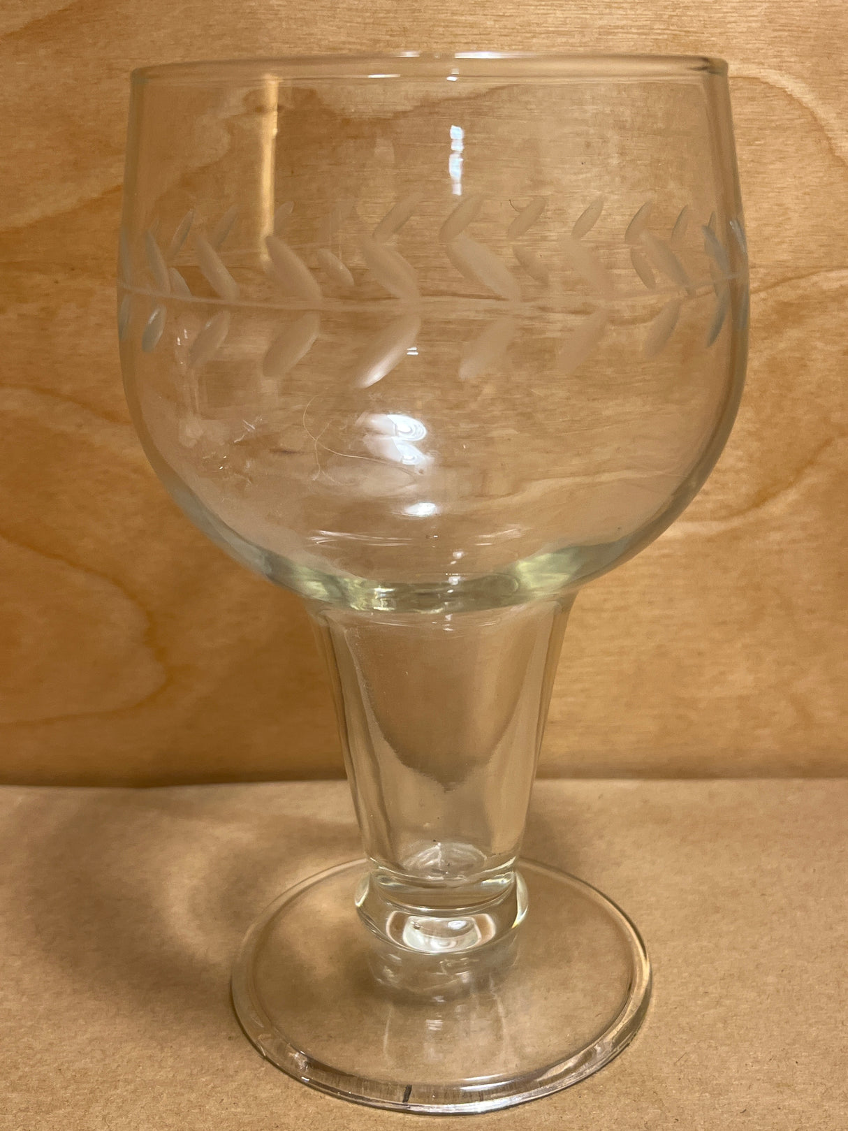 Laurel gray cut glass goblet with a frosted leaf motif, featuring a short flared stem and round foot, set against a wooden backdrop.