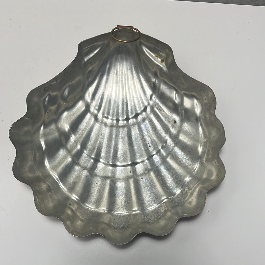 A large copper seashell baking pan with nickel lining with a removable bottom rests on a white surface in the kitchen.