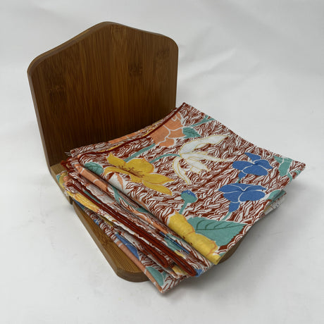 Adjustable bamboo napkin holder holding a stack of cloth napkins with flower details. From Spoons Kitchen Exchange. 