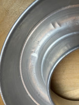 Circular Bundt pan - vintage aluminum for baking or Jello, featuring smooth contours on a wooden surface, highlighting its lightweight design and minor dings.