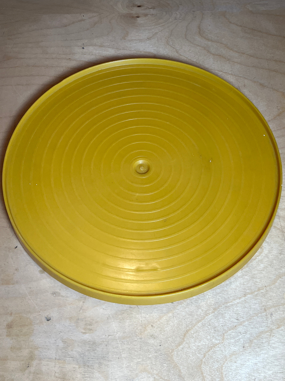 Bee Plastics harvest gold lazy Susan tray, a circular disk with concentric ridges and a central raised boss, resting on a wooden surface.
