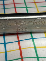 Close-up of Vollrath 4791620 stainless steel serving tongs handle, featuring NSF mark and leaf symbol, resting on patterned cloth.