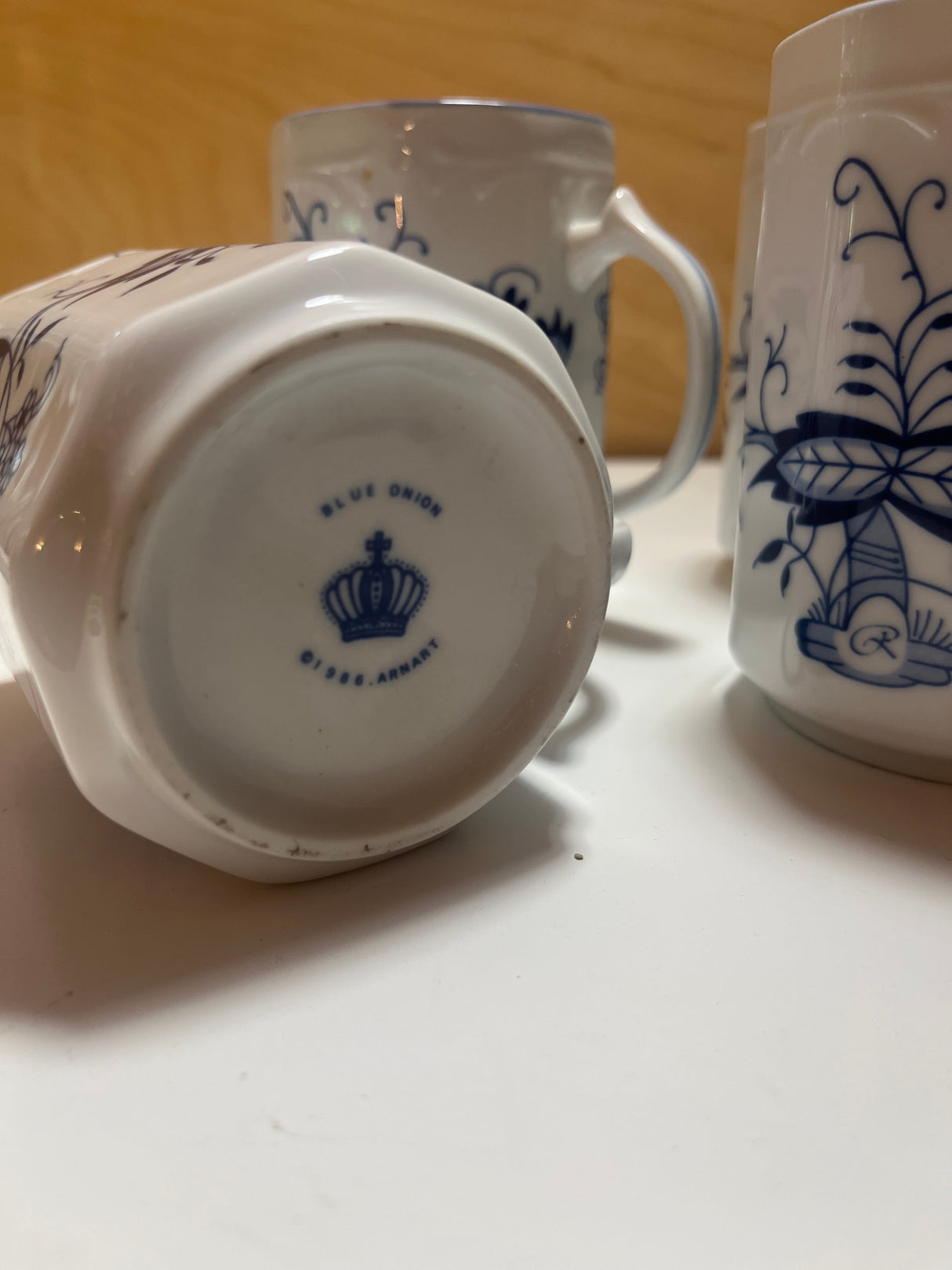 1986 Arhnart set of 4 Blue Onion coffee mugs features florid blue illustrations, embossed floral rims, ornate handles, and angular sides on glossy white ceramic.