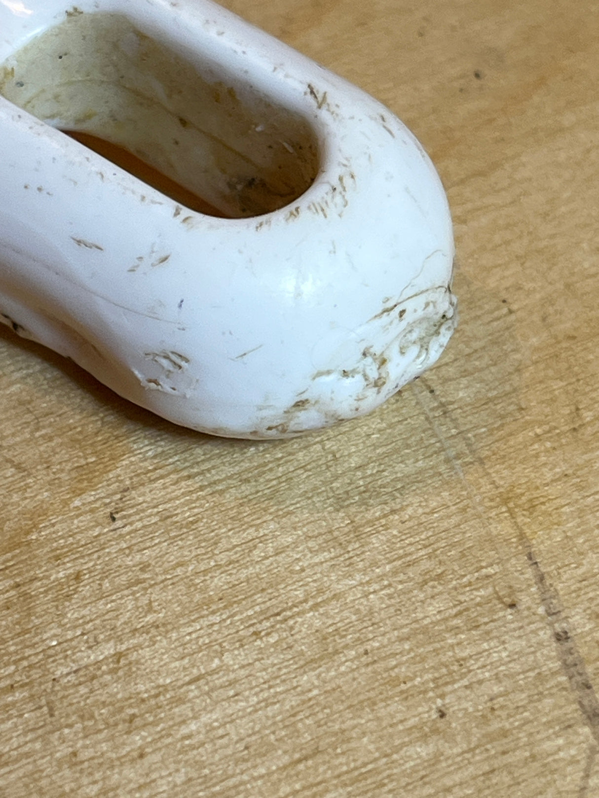 Round skimmer spoon with stainless steel head and white plastic handle, showing minor heat damage on the tip. Visible scuff marks and grime on the handle.