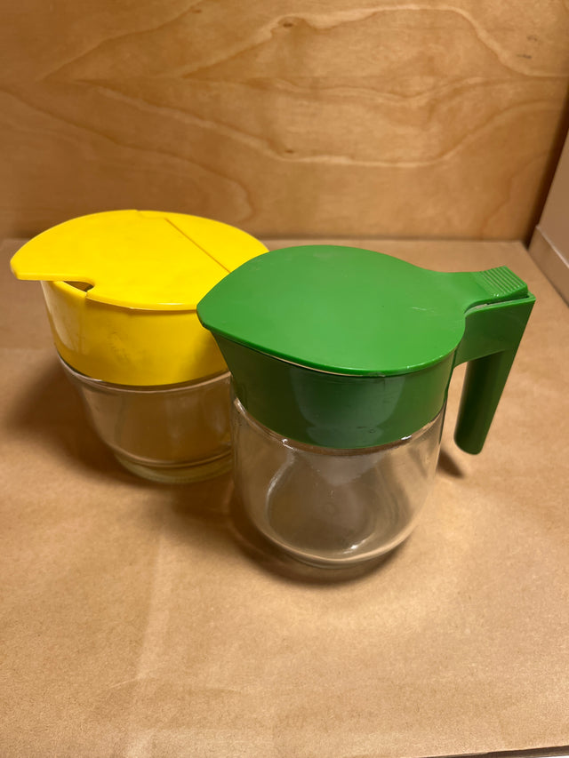 Gemco sugar and cream dispenser set, featuring two clear glass jars with flip-on lids, one with a handle, ideal for syrup or creamer.