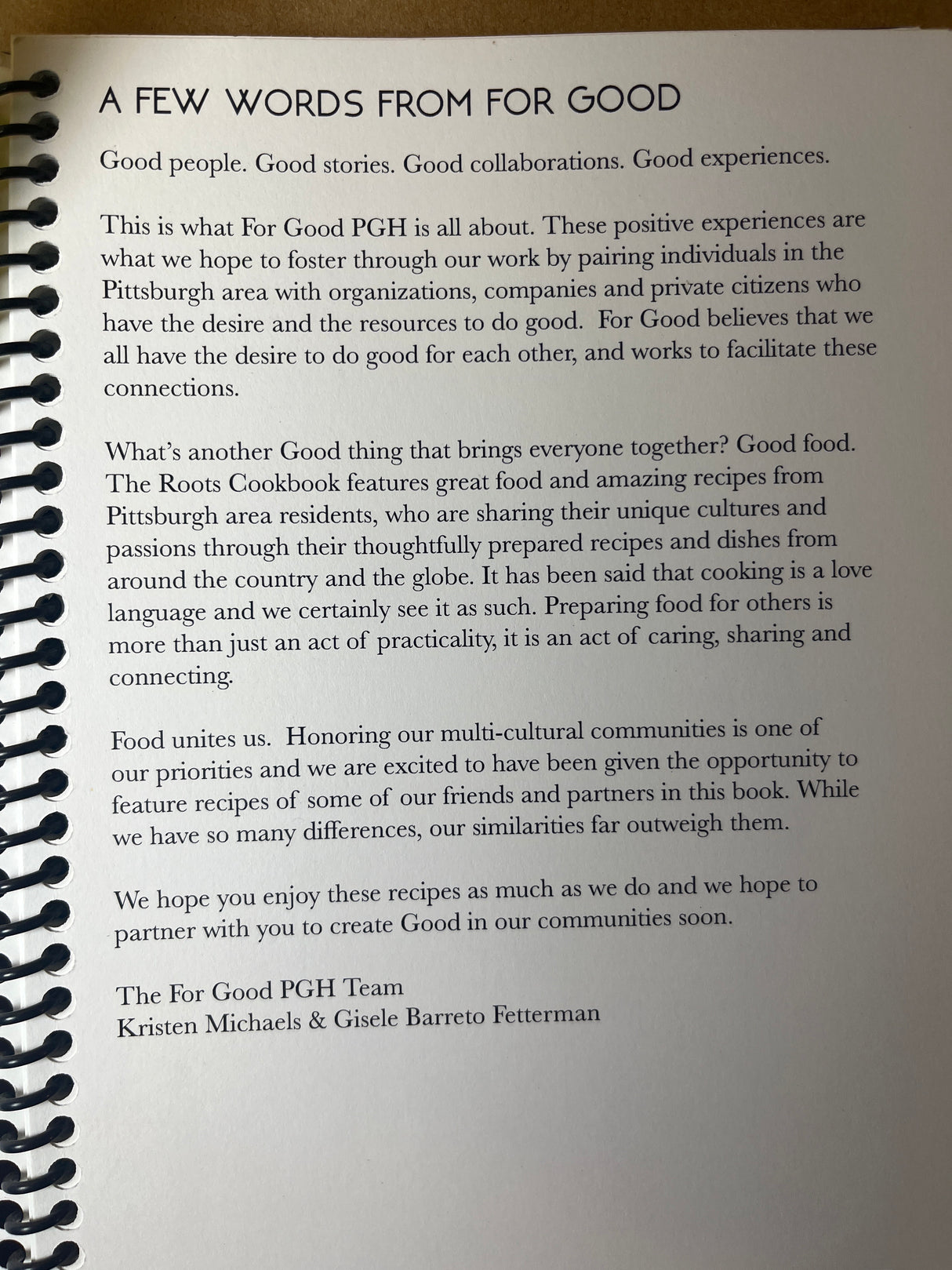 Spiral-bound Roots Cookbook page with a For Good PGH note detailing their mission of community connection through cultural recipes, signed by Kristen Michaels & Gisele Barreto Fetterman.
