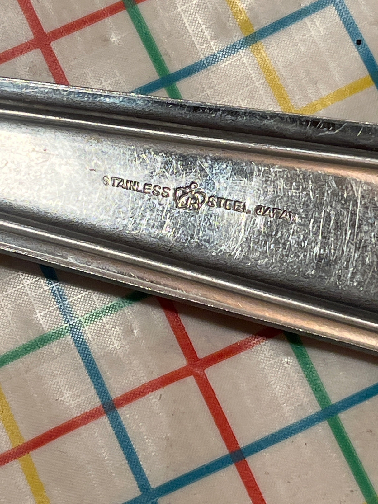 Extra long slotted basting spoon - JR stainless steel, showcasing a stamped handle, ideal for heat protection and durability, resting on a patterned tablecloth.