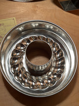4-piece springform pan set by Pampered Chef, featuring a shiny, fluted Bundt-style cake pan on a wooden surface, partially covering a small paper flyer.
