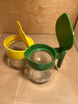 Gemco sugar and cream dispenser set featuring two small glass jars with flip-top lids, one green and one yellow, ideal for pourable condiments.