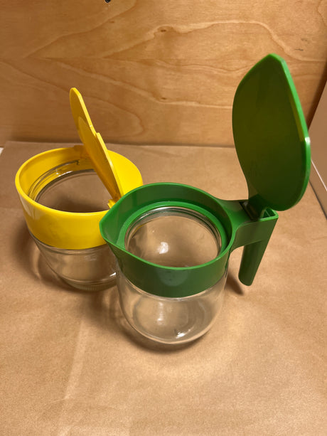 Gemco sugar and cream dispenser set featuring two small glass jars with flip-top lids, one green and one yellow, ideal for pourable condiments.