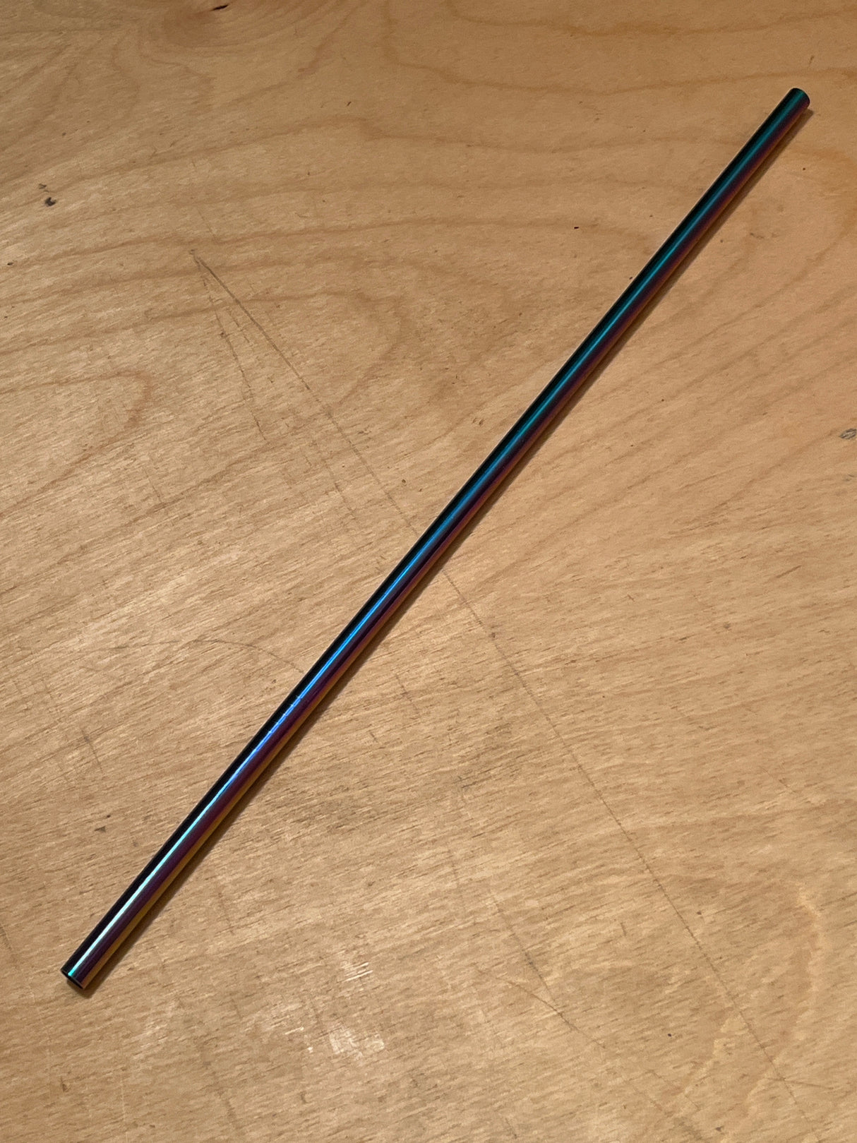 Stainless steel reusable drinking straw with an iridescent finish, placed diagonally on a wood-grain surface, showcasing its sleek, eco-friendly design.