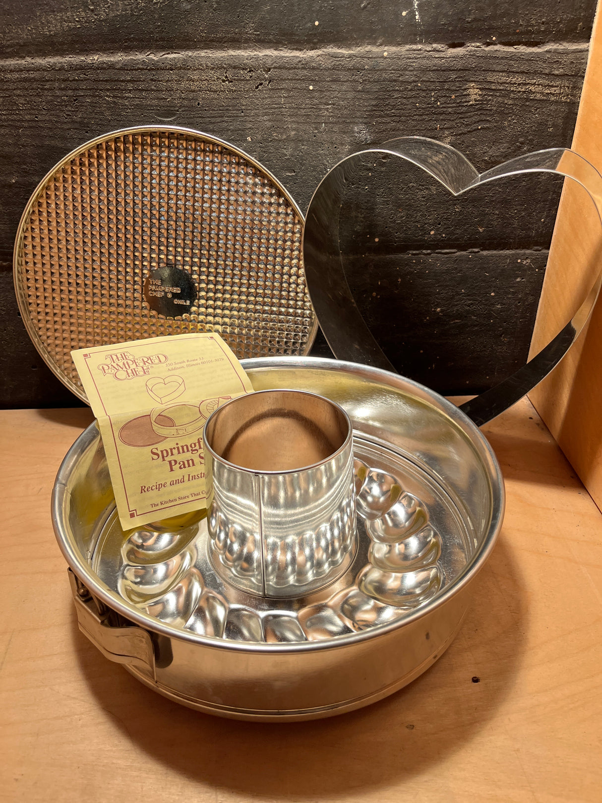 4-piece springform pan set - Pampered Chef: includes a round pan with latch, fluted tube insert, removable textured base, heart-shaped insert, and instruction booklet.