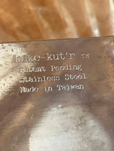 Square Kake-kut’r close-up showing metal stamp details: “kake-kut’r™,” “Patent Pending,” “Stainless Steel,” “Made in Taiwan.” Ideal for easy one-handed dessert serving.