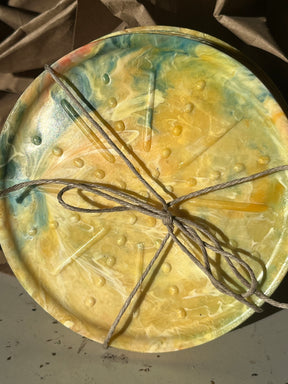 Coaster Sets from Reimagined Recycling: A round, marbled platter with embossed texture, tied with twine on crumpled packing paper, showcasing handmade recycled craftsmanship.