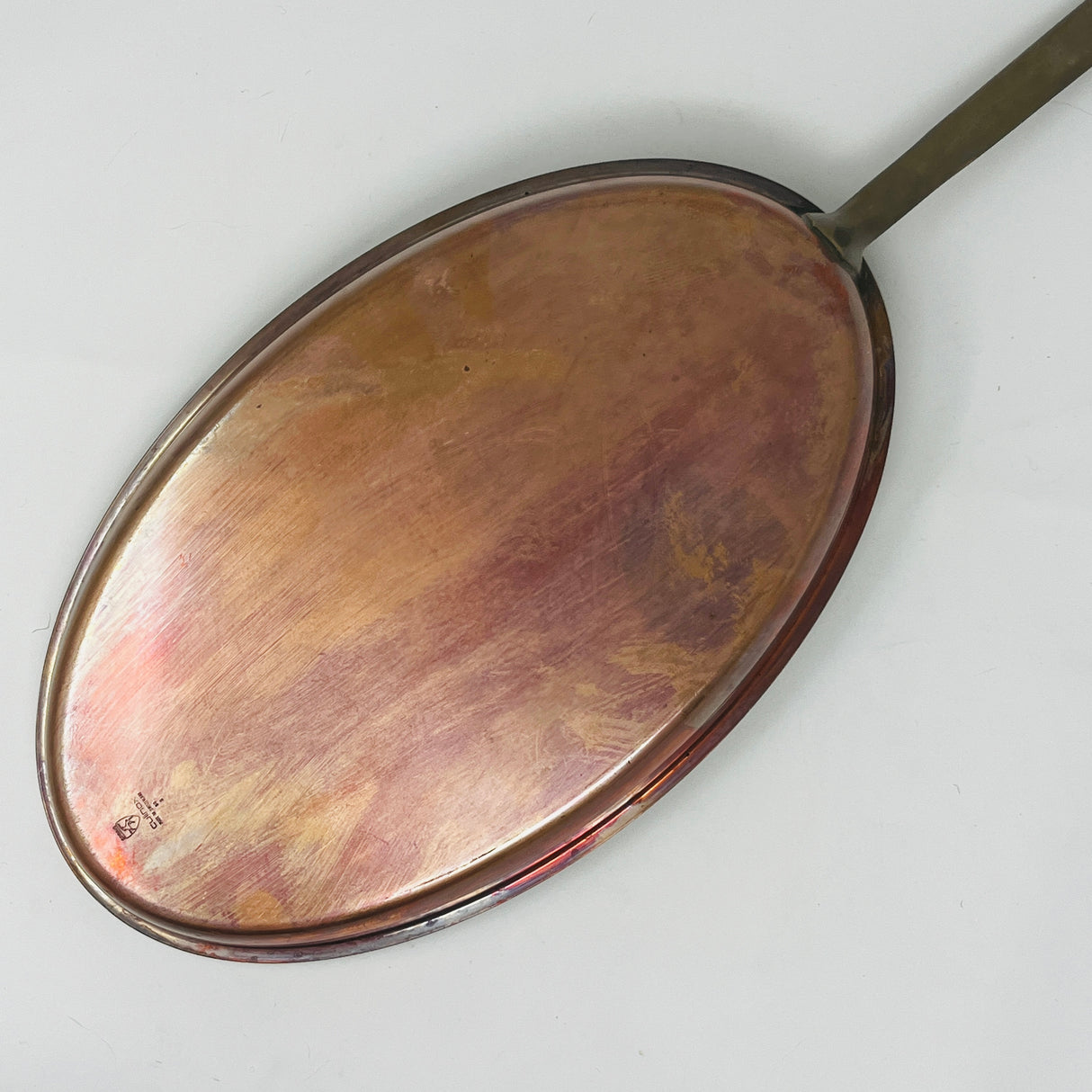 A polished stainless steel pan with a long, slender handle,copper base is reflecting the light, on a white background. From Spoons Kitchen Exchange.