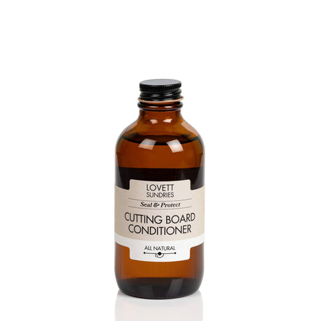 Small amber-glass bottle labeled Coconut Oil Cutting Board Conditioner by Lovett Sundries, featuring a black screw-top lid, designed for conditioning wooden kitchenware with all-natural coconut oil.