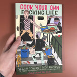 Cover of Cook Your Own Fucking Life: Vegan Comfort Food Recipes by Ashley Rowe Palafox, featuring an illustrated punk scene and subtitle emphasizing community and veganism.