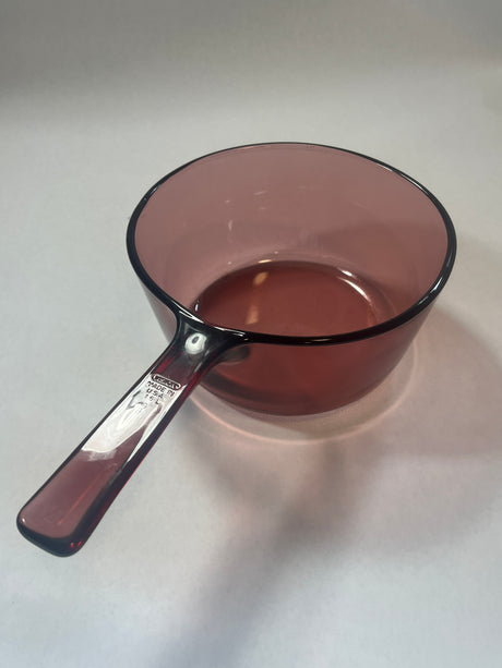 Cranberry Vision Ware pot by Pyrex with a handle and lid, suitable for stove and oven use, featured alongside a spoon and glass bowl.